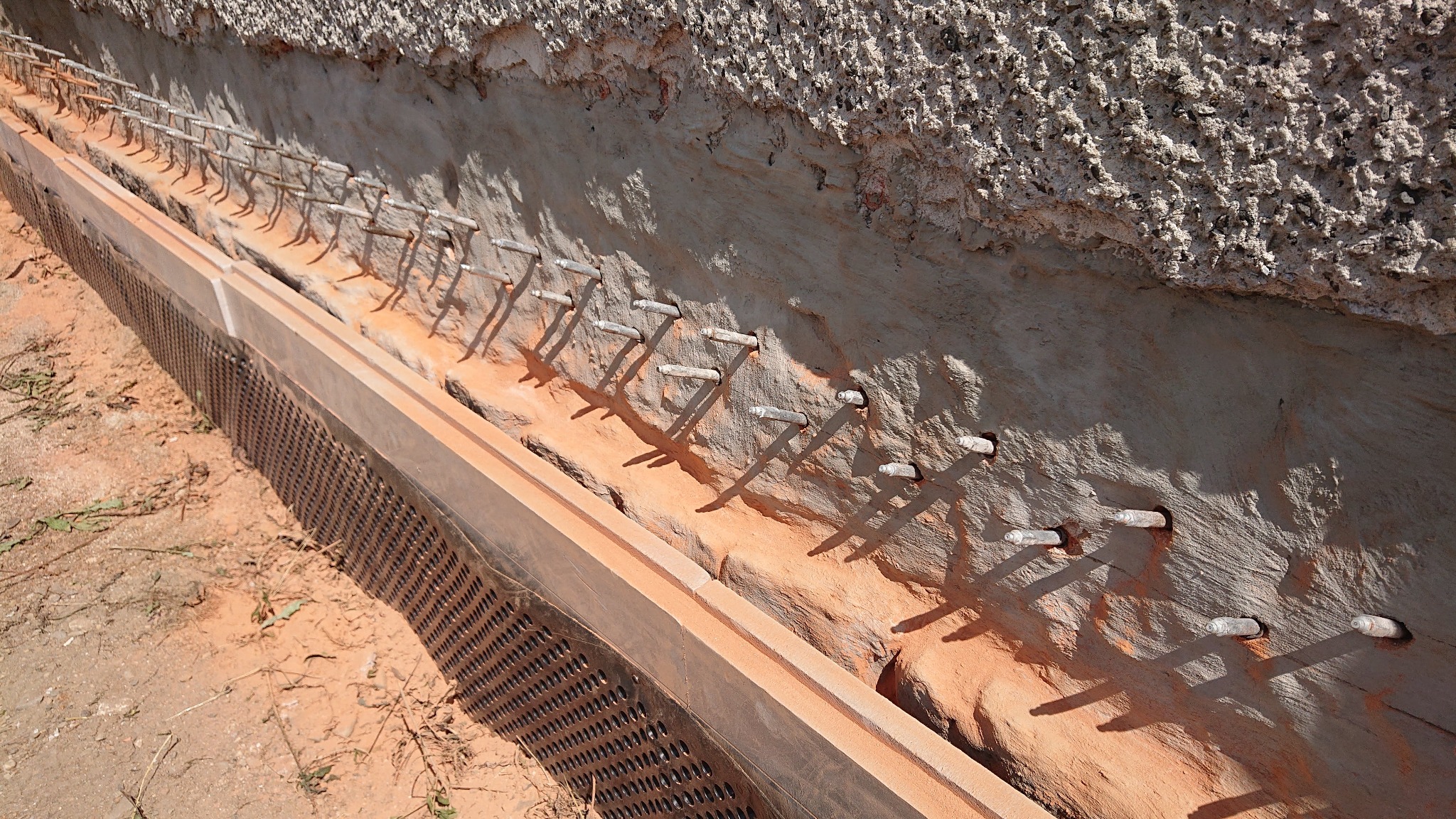 Przygotowanie wykopu pod fundamenty z widocznymi kotwami w ścianie i perforowaną płytą ochronną, grunt piaszczysty.