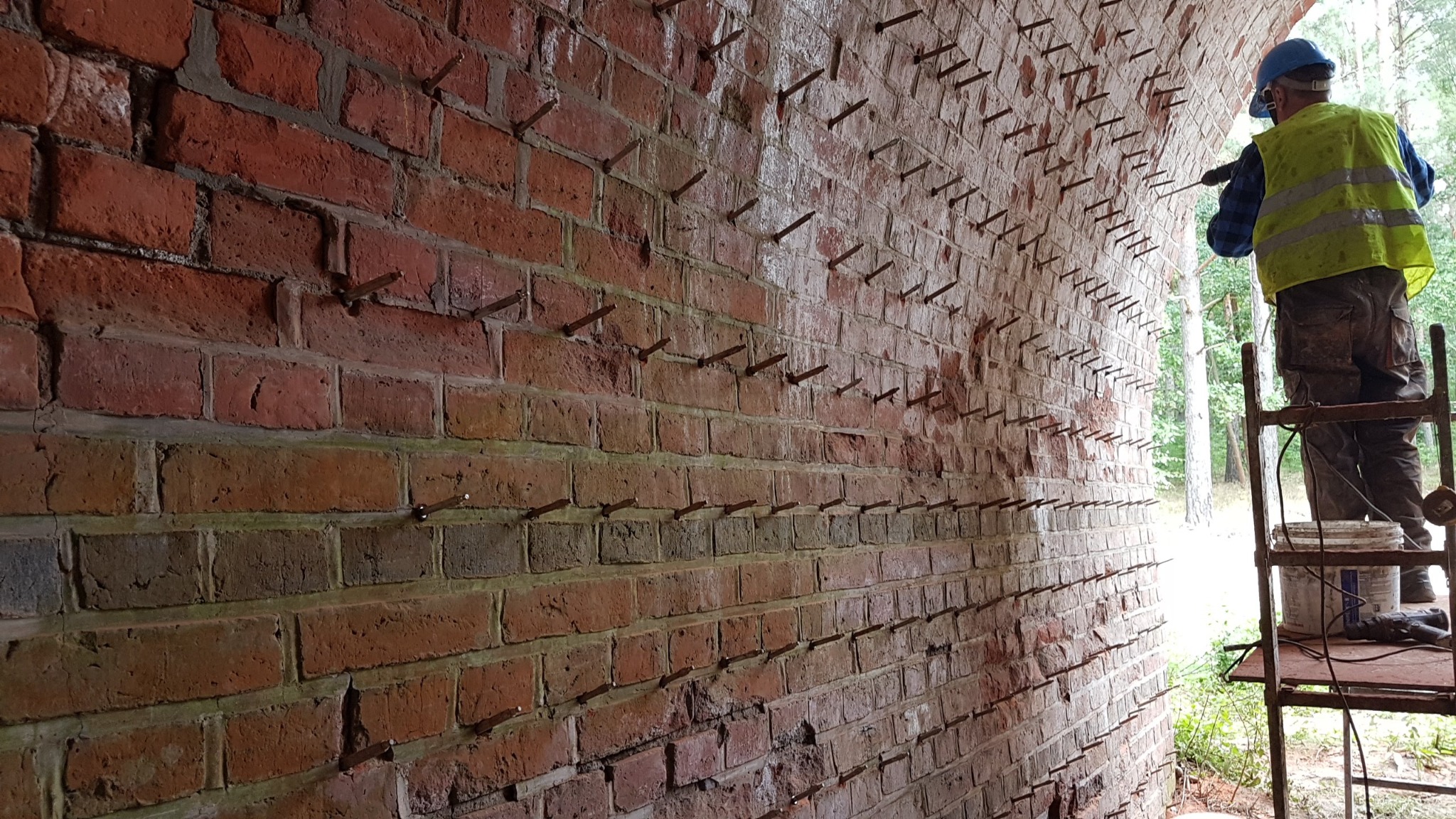 Prace przy wzmacnianiu ceglanego sklepienia w Sulęcinie, widoczne liczne metalowe kotwy i pracownik wiercący otwory pod kolejne.