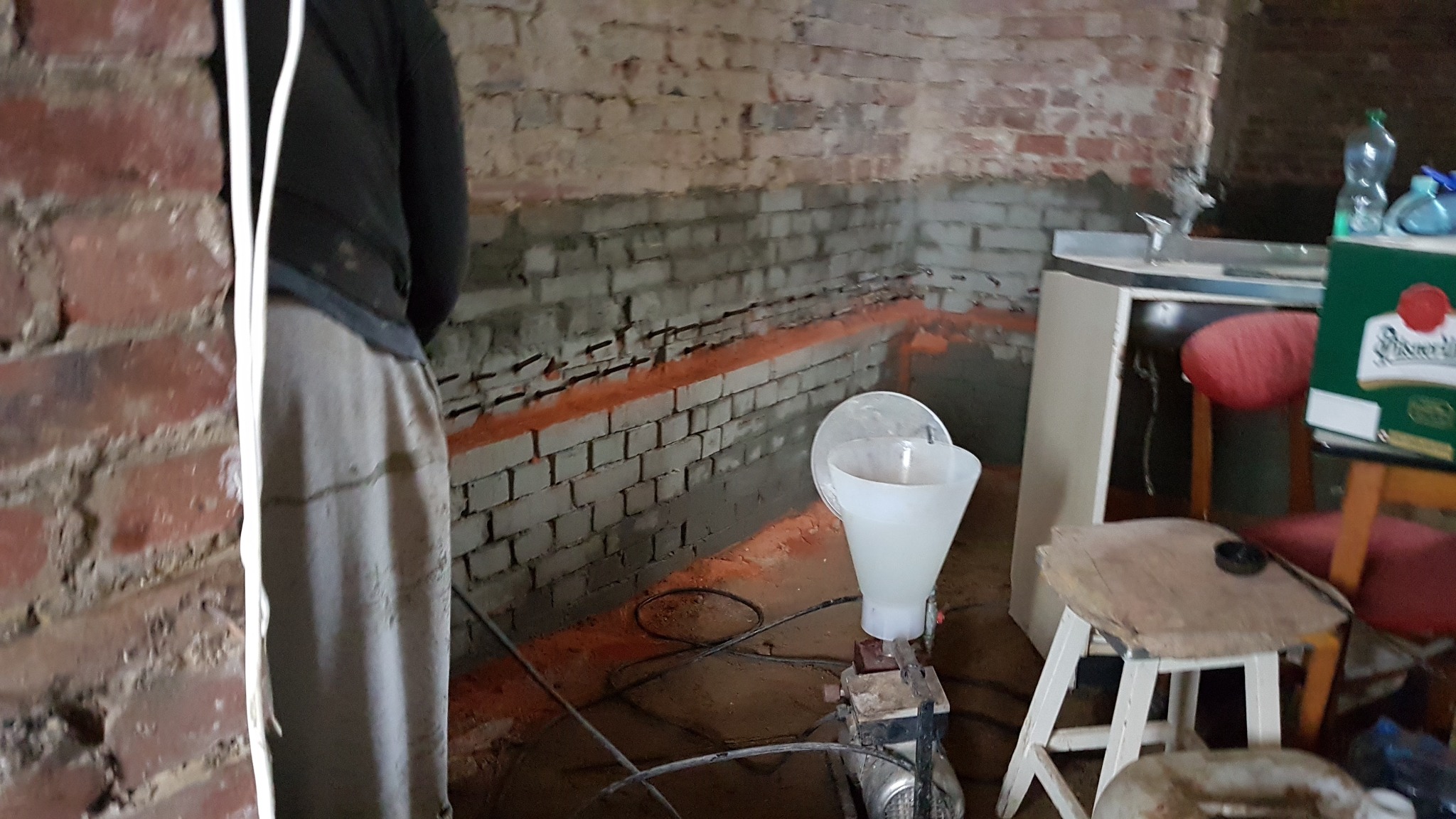 Przygotowanie do iniekcji poziomej w murze z cegły, widoczny sprzęt do iniekcji oraz nawiercone otwory wypełnione preparatem uszczelniającym.