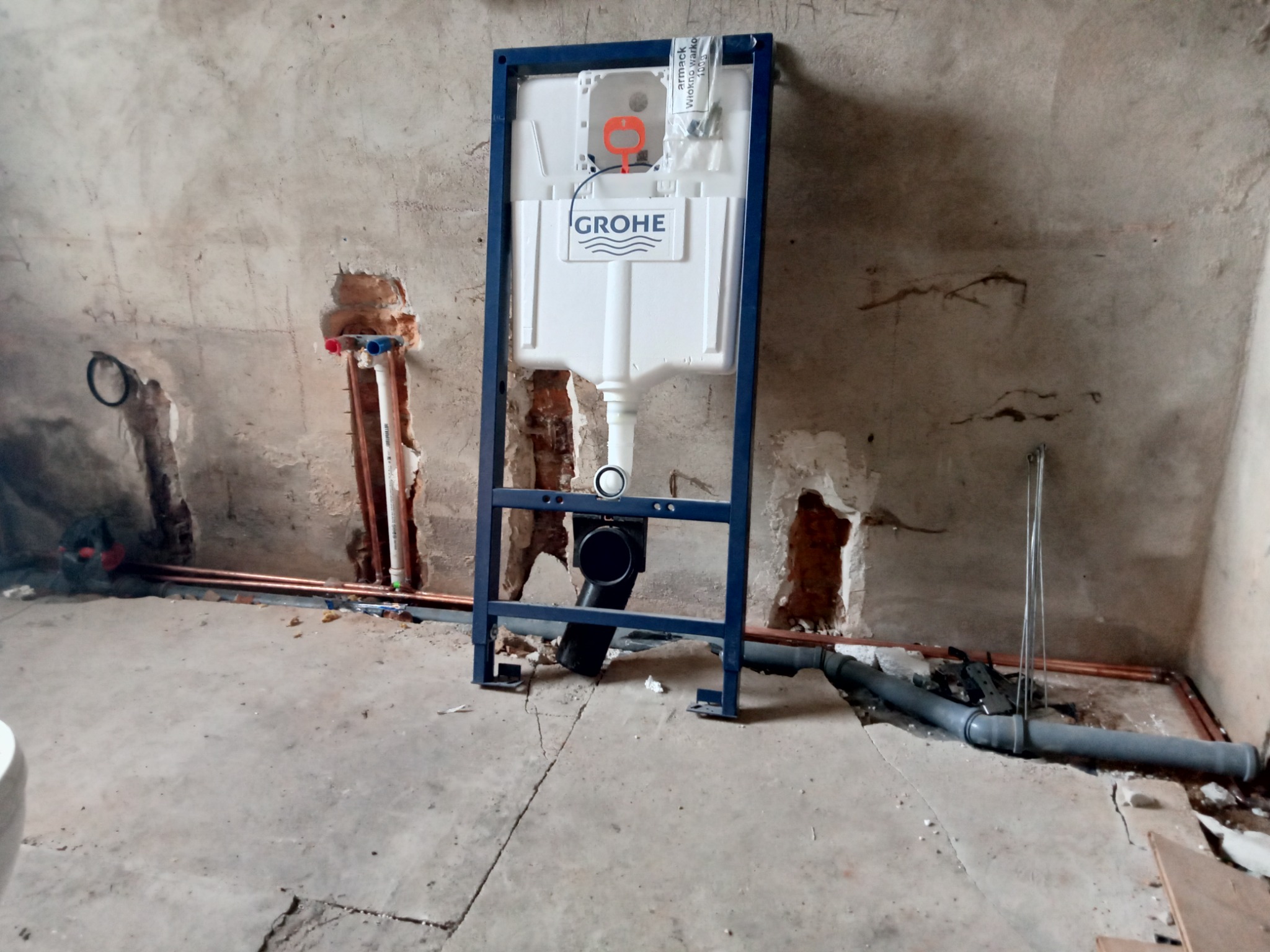 Stelaż podtynkowy Grohe zamontowany przy surowej ścianie z widocznymi instalacjami hydraulicznymi i kanalizacyjnymi w trakcie remontu łazienki.