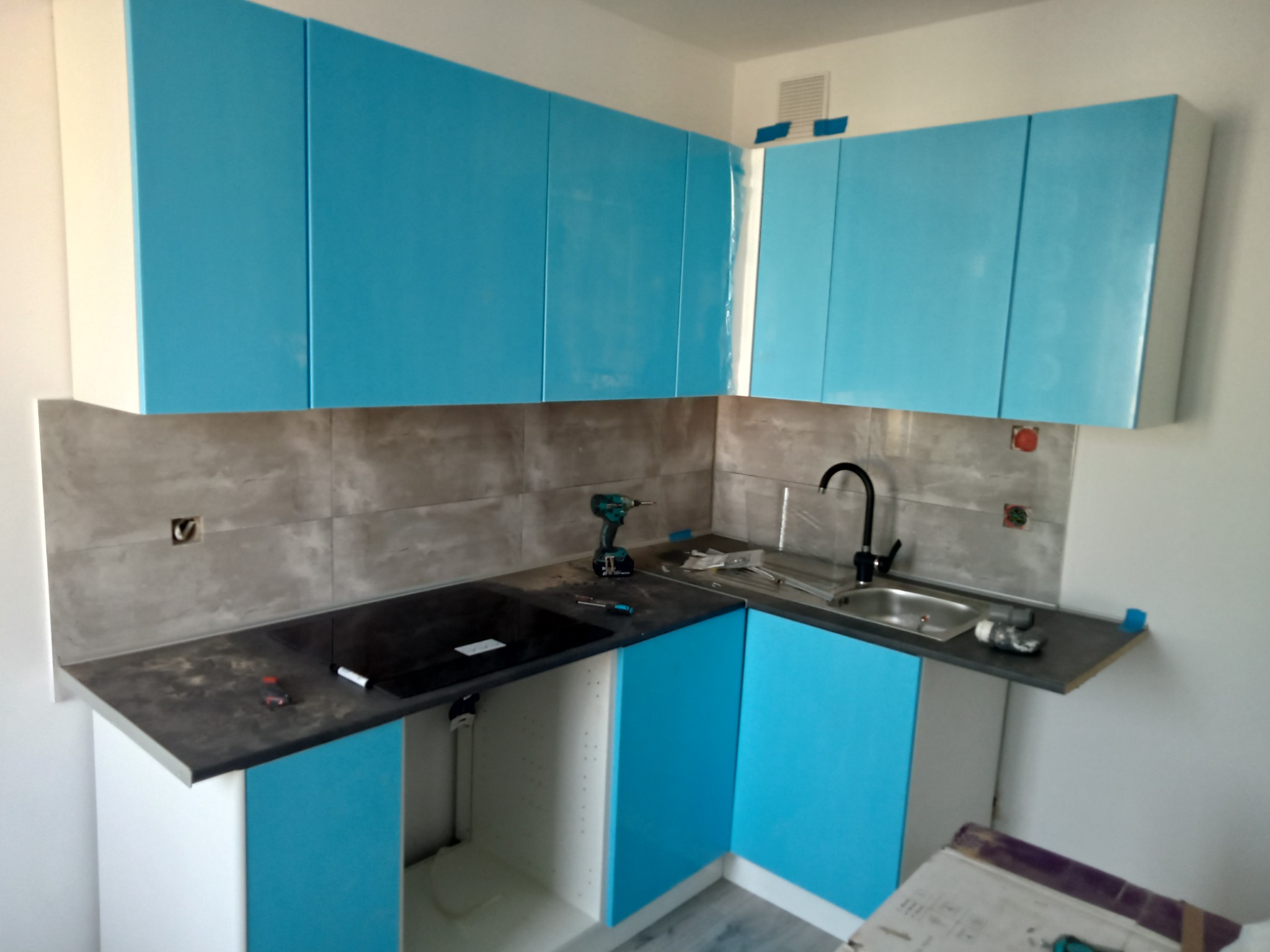 Montaż błękitnej zabudowy kuchennej w Witnicy: widoczne szafki górne i dolne, czarny blat, płyta indukcyjna, zlewozmywak, oraz narzędzia monterskie sugerujące trwający proces instalacji.