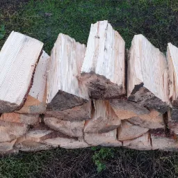 Stos pociętego drewna na tle zielonej trawy, widoczne sęki i struktura drewna.