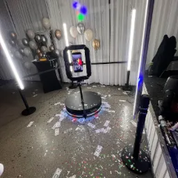 Obracająca się platforma z oświetleniem i ekranem, na podłodze rozsypane konfetti i rekwizyty w postaci banknotów dolarowych, w tle balony i białe zasłony.