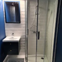 Nowoczesna łazienka z kabiną prysznicową, umywalką nablatową na szafce w kolorze granatowym oraz wzorzystą podłogą w odcieniach szarości i zieleni.