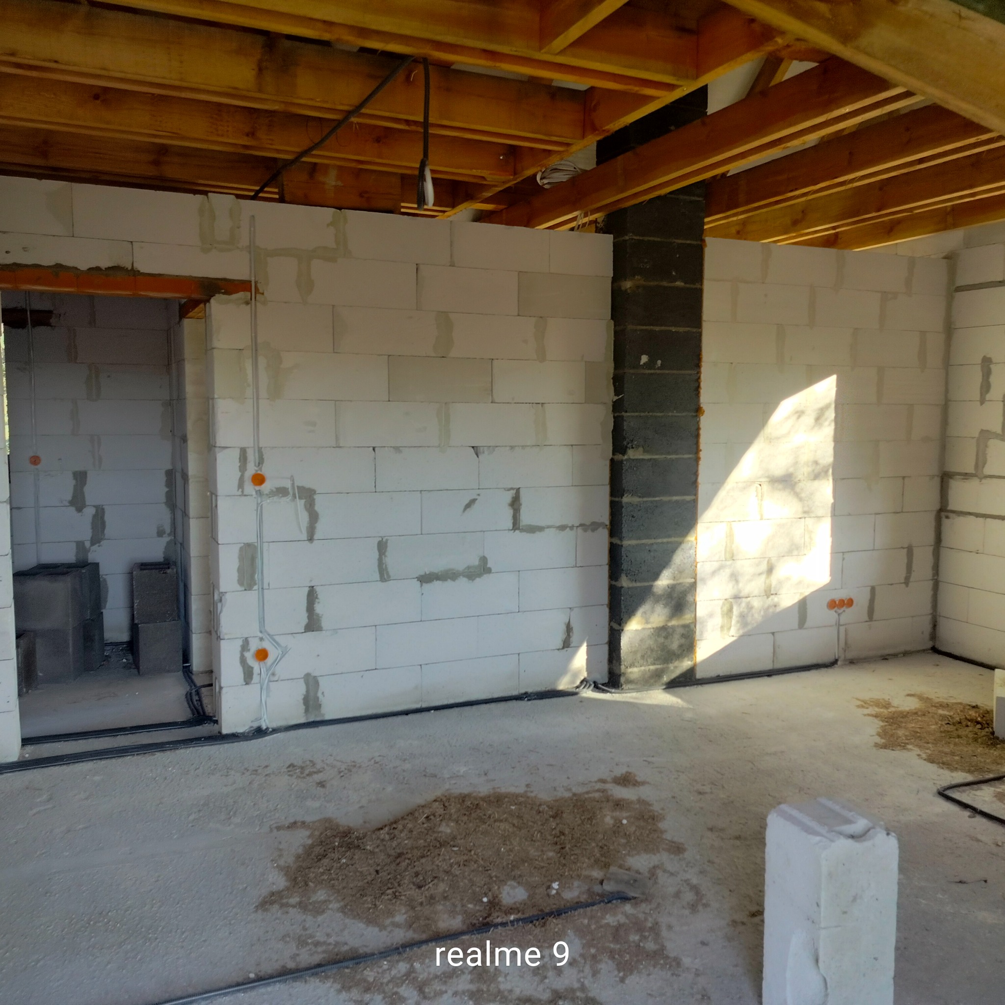 Surowy stan wnętrza z instalacją elektryczną w rurkach podtynkowych, ściany z betonu komórkowego, drewniany strop, widoczne puszki instalacyjne.