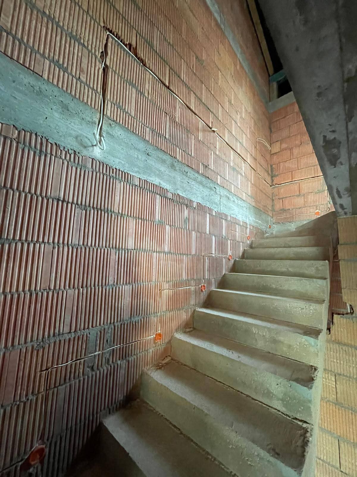 Surowa ściana z instalacją elektryczną w trakcie budowy schodów. Widoczne przewody i puszki elektryczne wmurowane w cegły. Kątowe ujęcie z dołu.