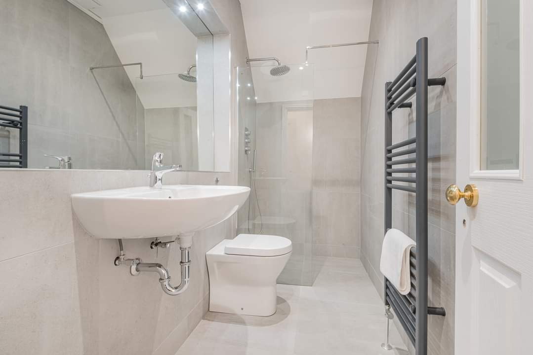 Jasna łazienka z kabiną prysznicową, umywalką nablatową, grzejnikiem drabinkowym i szarymi płytkami na ścianach.