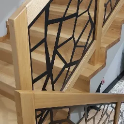 Drewniane schody z balustradą o geometrycznym, czarnym wzorze, widok z góry, jasne drewno.