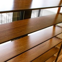 Owsiak Patryk Okna - Zbliżenie na drewniane żaluzje poziome w kolorze ciepłego brązu, częściowo otwarte, z widocznym wzorem słojów drewna i delikatnym światłem wpadającym z zewnątrz.