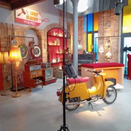 Żółty skuter na planie filmowym z rekwizytami retro, oświetleniem studyjnym i dekoracjami w tle, w tym znak 'Łowcy Skarbów'.