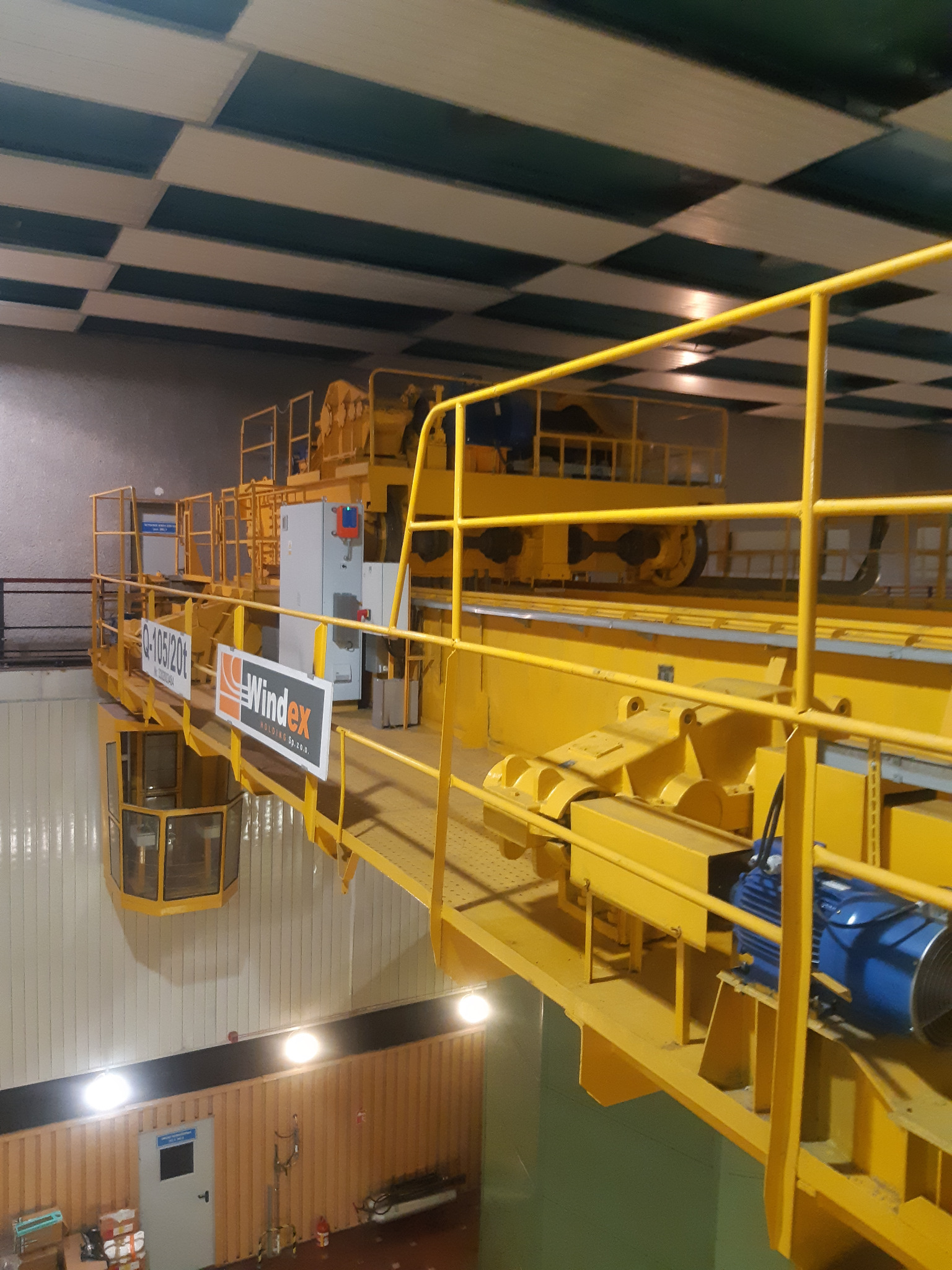 Żółty suwnica pomostowa z napisem 'Windex' i parametrami 'Q-105/20t' w hali przemysłowej z kasetonowym sufitem.