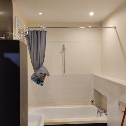 Mieć-Dom - Nowoczesna łazienka z wanną, szarą zasłoną prysznicową z akcentami turkusowymi i czarnymi płytkami pod wanną, oświetlona trzema punktowymi lampami.