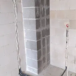 Wnętrze w trakcie prac instalacyjnych: ułożone w peszlach kable elektryczne przy ścianie z betonu kom&oacute;rkowego, widoczne narzędzia i elementy mocujące.