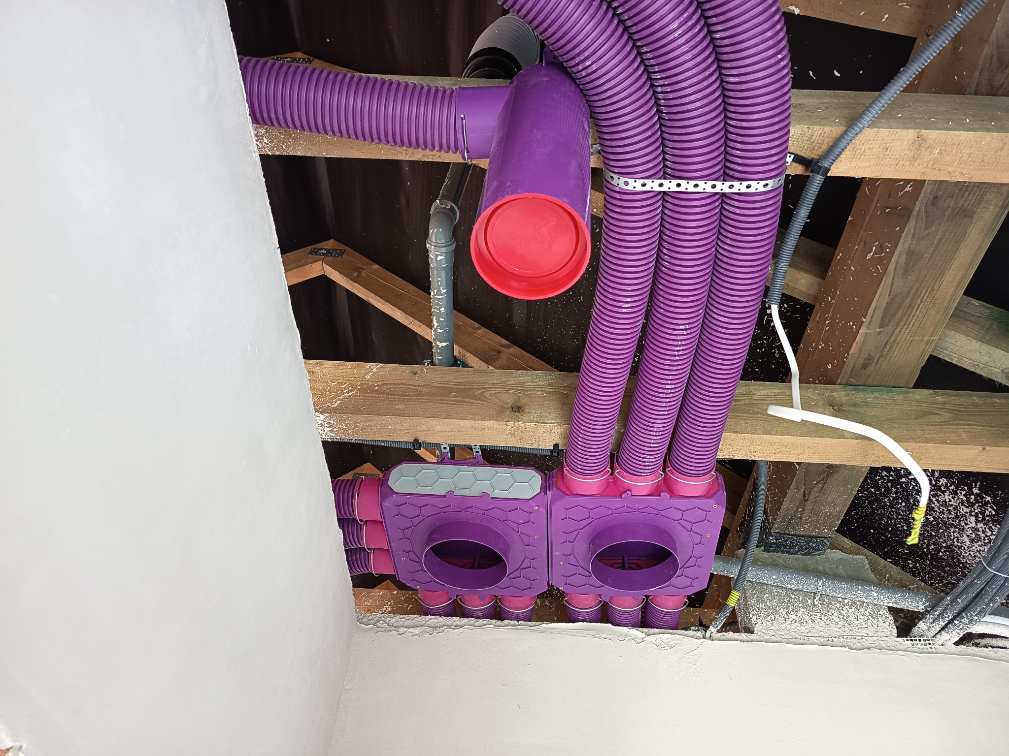 Fioletowe rury wentylacyjne zamontowane pod stropem, widoczne elementy instalacji i drewniana konstrukcja dachu. Nietypowy kolor instalacji wentylacyjnej.