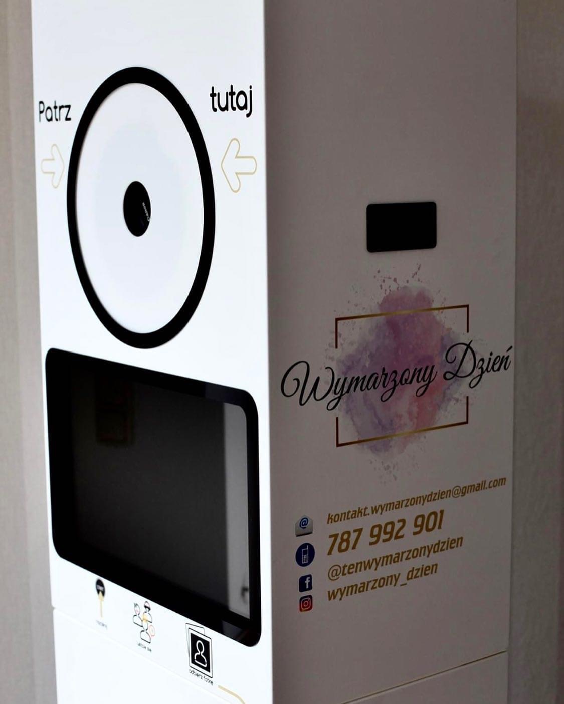 Biała fotobudka z instrukcją 'Patrz tutaj' i logotypem 'Wymarzony Dzień' wraz z danymi kontaktowymi.