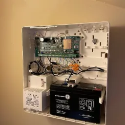 Otwarta obudowa centrali alarmowej Satel Perfecta 32 LTE z widoczną płytą główną, transformatorem Pulsar AWT150 i akumulatorem Securbat, zamontowana na beżowej ścianie.