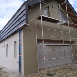 PUH Michał Zulczyk - Nowo otynkowany dom jednorodzinny z ciemną dachówką, widoczne rusztowanie i zabezpieczone okna folią ochronną.