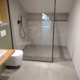 Nowoczesna kabina prysznicowa typu walk-in z czarną ramą i deszczownicą w łazience na poddaszu z szarą płytką podłogową i ścienną.