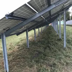 Rząd paneli słonecznych na metalowej konstrukcji, widok od dołu, trawa wokół świeżo skoszona.