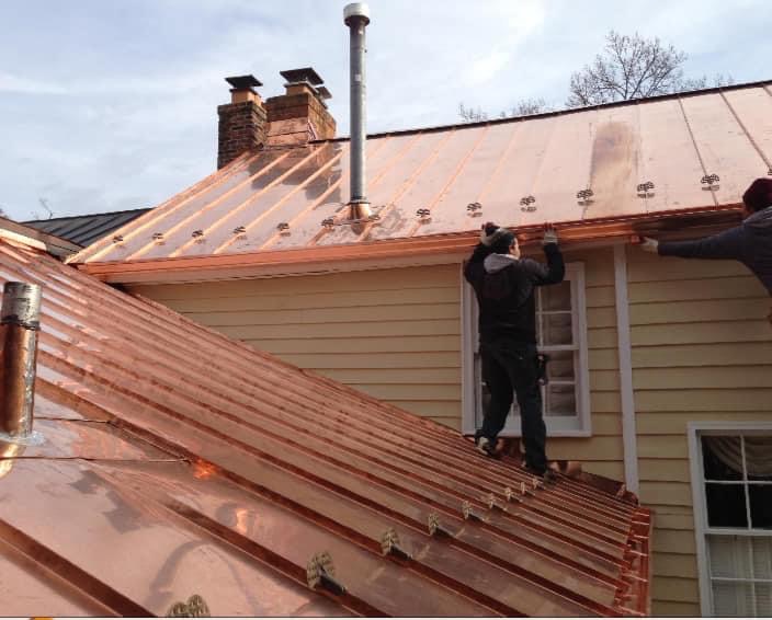 Montaż miedzianych rynien na tle żółtej elewacji domu, widoczne elementy dachu i komin