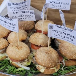 Vegas Grzegorz Wiśniowski - Mini burgery z sezamem na tacy, ozdobione flagami Pizzeria Vegas, prezentacja cateringu na imprezę firmową. Widok z bliska, skupienie na detalach.