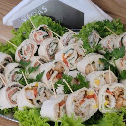 Vegas Grzegorz Wiśniowski - Elegancko podane roladki tortilli z różnymi nadzieniami (łosoś, kurczak) na srebrnej tacy, udekorowane sałatą i ziołami. Szpilki utrzymują zwinięte kawałki.