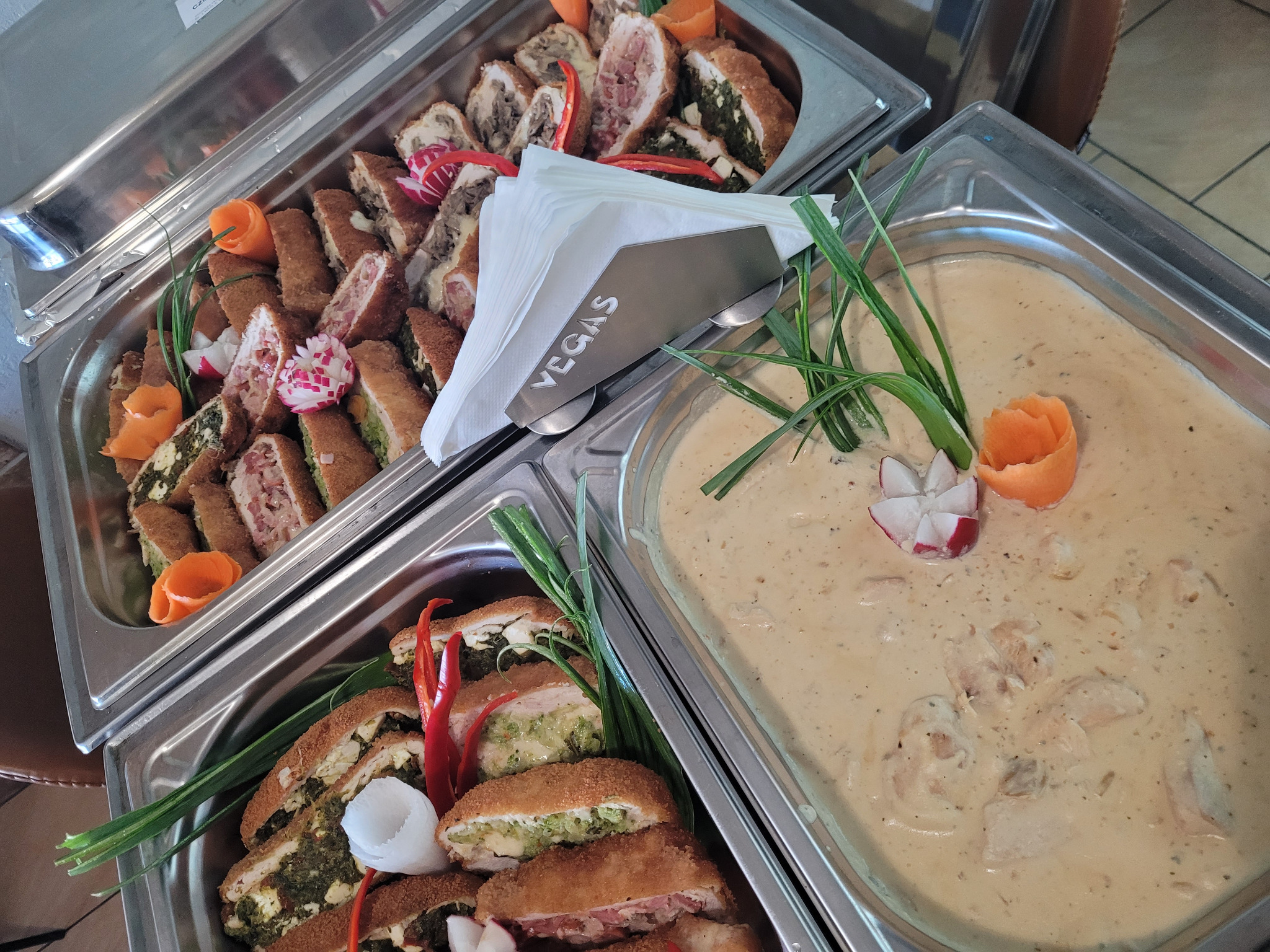 Dwa metalowe bemary wypełnione dekoracyjnie ułożonymi roladkami z różnym nadzieniem i sosem, ozdobione warzywami. Na jednym z bemarów widoczny napis Vegas.