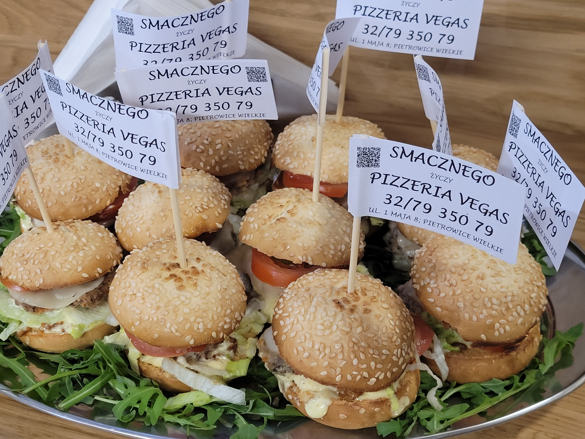 Mini burgery z sezamem na tacy, ozdobione flagami Pizzeria Vegas, prezentacja cateringu na imprezę firmową. Widok z bliska, skupienie na detalach.