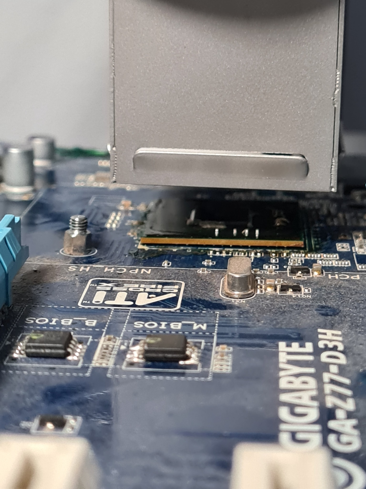 Zbliżenie na zakurzoną płytę główną komputera Gigabyte GA-Z77-D3H z widocznym radiatorem chipsetu, elementami BIOS i oznaczeniami ATI CrossFireX.