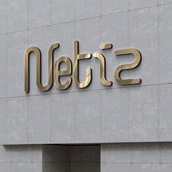 Złoty, metaliczny napis 'Netiz' na szarej, teksturowanej ścianie z płytek.