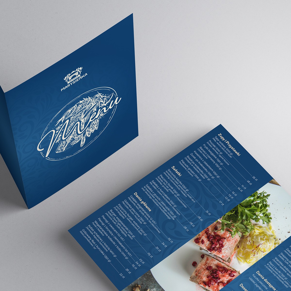 Rozłożone menu restauracji 'Marysieńka' z logo, prezentujące dania i ceny, ustawione pod kątem na jasnym tle.
