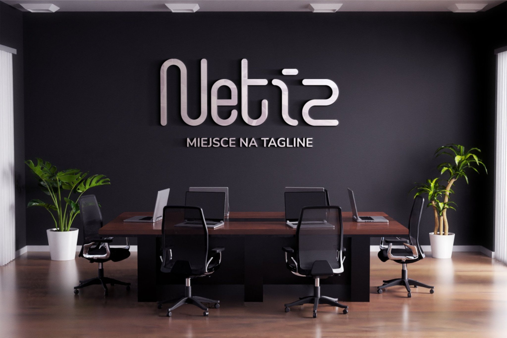 Nowoczesne biuro z ciemną ścianą, na której umieszczono srebrne logo firmy 'Netia' z napisem 'Miejsce na tagline', stół konferencyjny z laptopami i krzesłami biurowymi, oraz dwie rośliny doniczkowe...