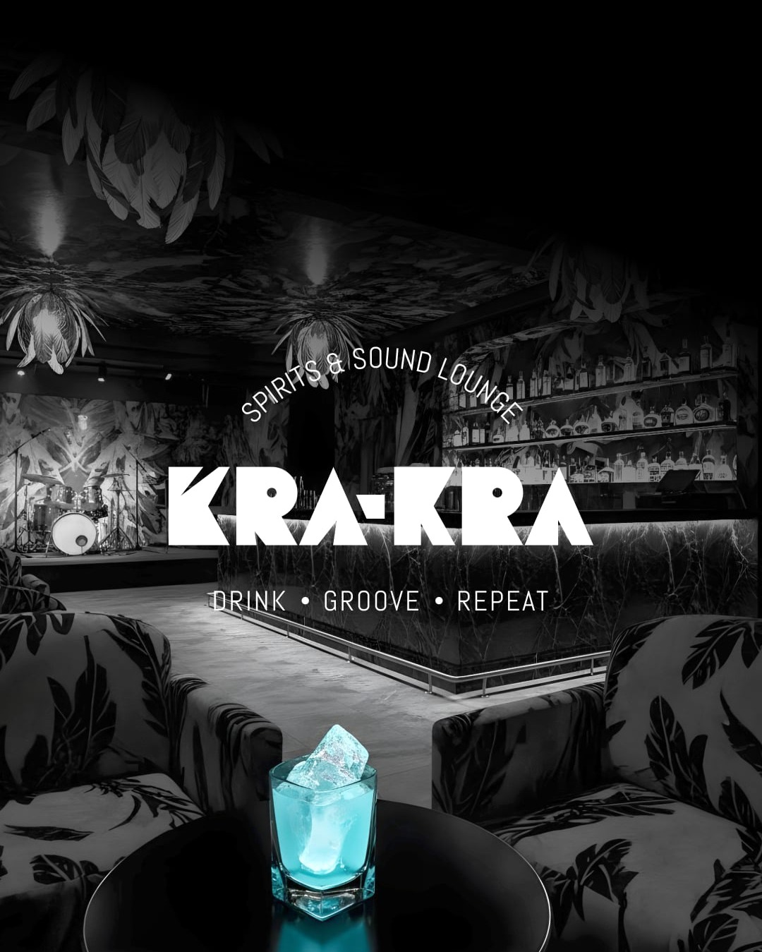 Stylowe wnętrze baru 'KRA-KRA' w odcieniach szarości z akcentem błękitnego drinka na pierwszym planie. W tle scena z perkusją i półki z alkoholami.