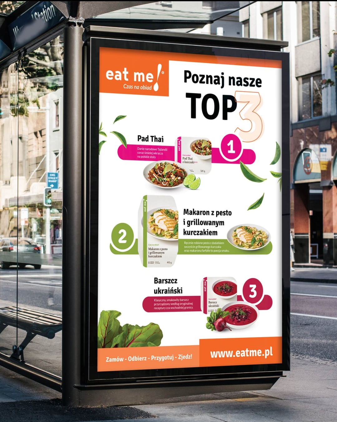 Billboard z ofertą dań gotowych Eat Me: Pad Thai, makaron z pesto i barszcz ukraiński. Reklama na przystanku autobusowym w miejskiej scenerii.