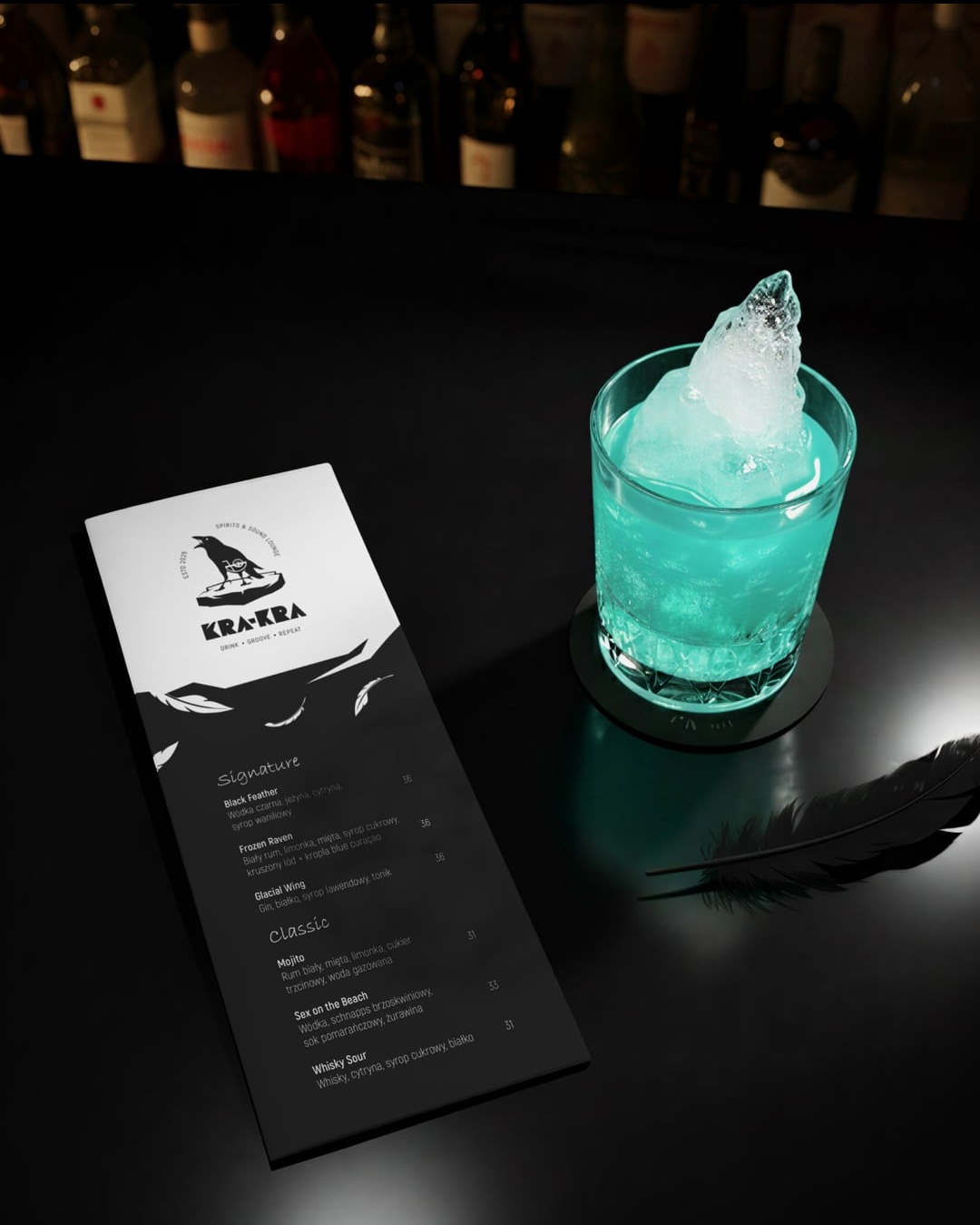 Turkusowy drink z kruszonym lodem obok menu KRA-KRA i pióra na czarnym tle. Elegancki bar z butelkami w tle. Minimalistyczna kompozycja.