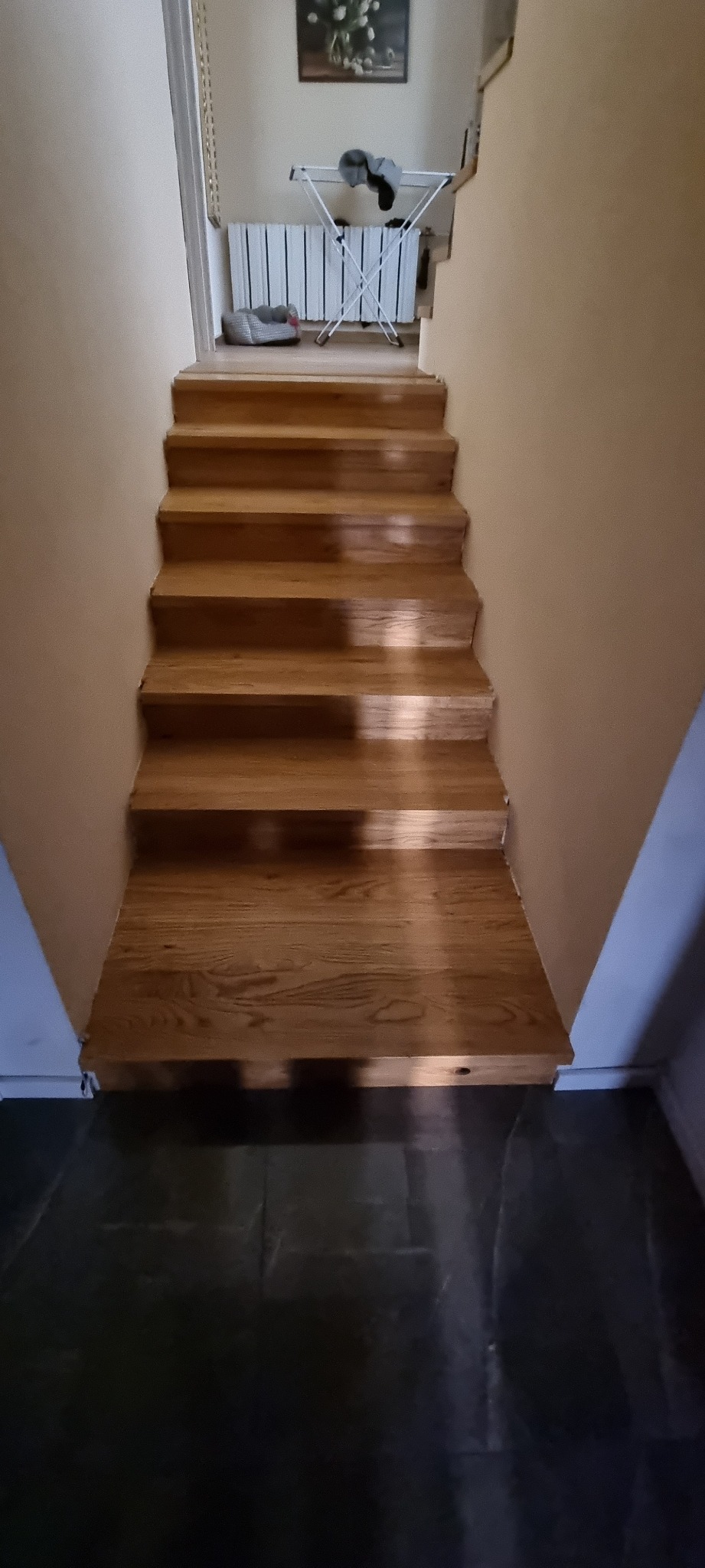 Schody drewniane w domu, widok z dołu, z widoczną suszarką na pranie i grzejnikiem w tle.
