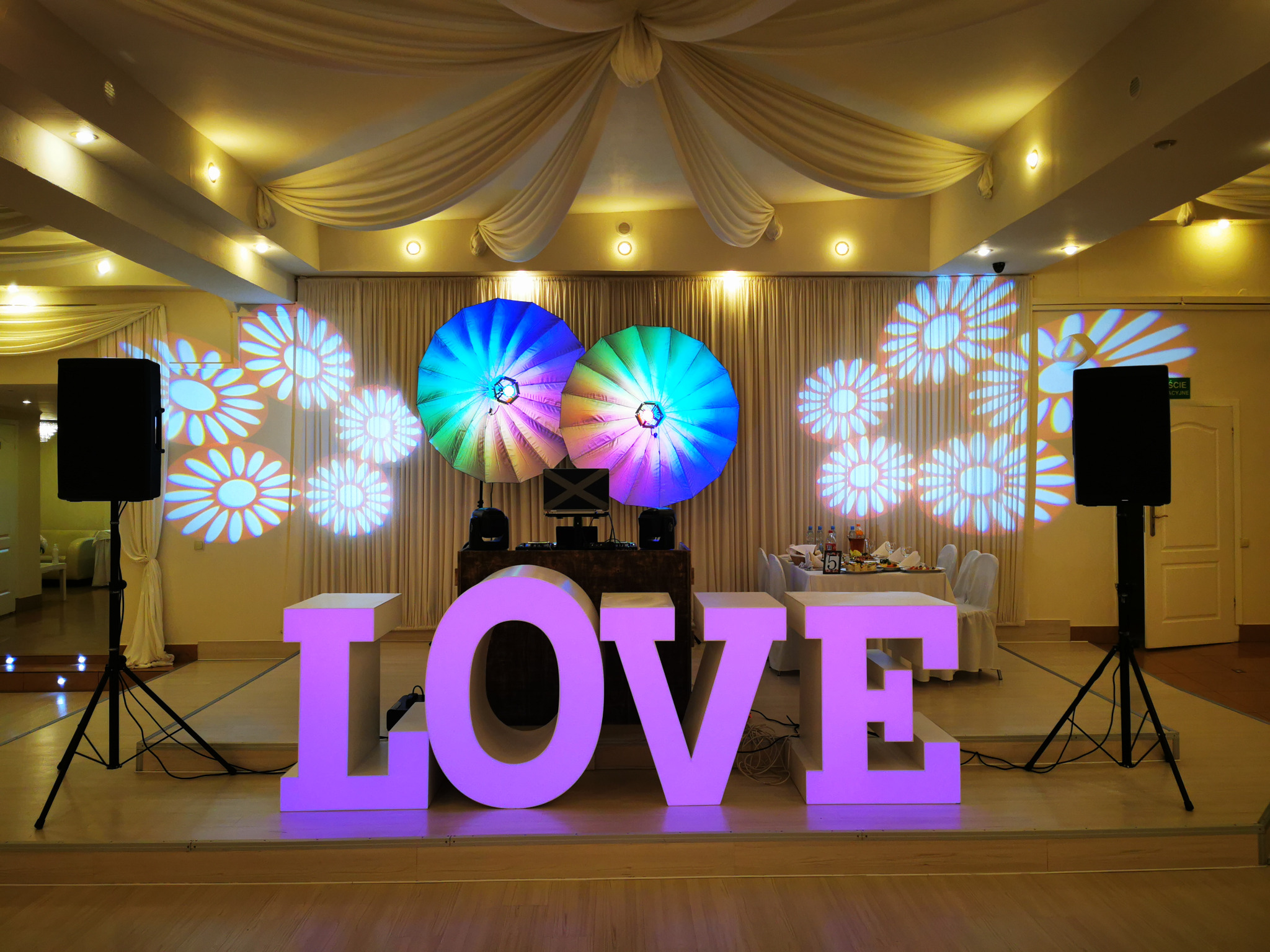 Dekoracja sali weselnej z podświetlanym napisem LOVE, oświetleniem dyskotekowym i projekcjami kwiatów na ścianach.