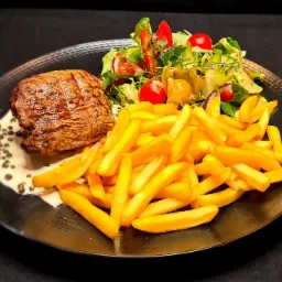 Stek wołowy z sosem pieprzowym, frytkami i sałatką z pomidorkami cherry oraz physalis na czarnym talerzu.