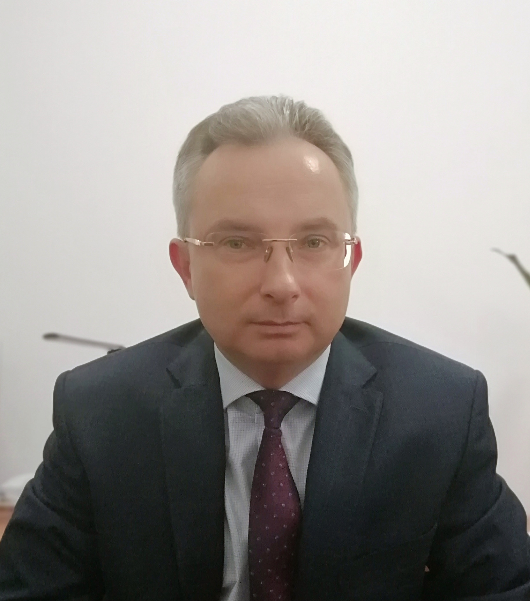 Portret biznesowy mężczyzny w okularach i garniturze, na neutralnym tle, z delikatnym uśmiechem.