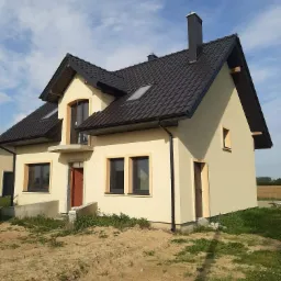 Niedawno wybudowany dom murowany w Kutnie z ciemną dachówką, kremową elewacją i widocznym fragmentem podwórka.