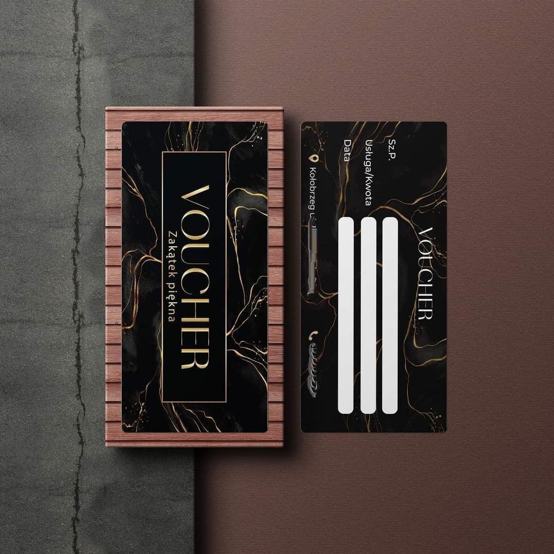 Elegancki, czarno-złoty voucher upominkowy w drewnianym etui, obok pusta karta vouchera z miejscem na wpisanie danych, na teksturowanym tle.