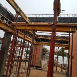 Wznoszenie ścian domu z bloczków, widoczne szalunki wzmacniające konstrukcję, stalowe podpory i zbrojenia, w tle zabudowa jednorodzinna.