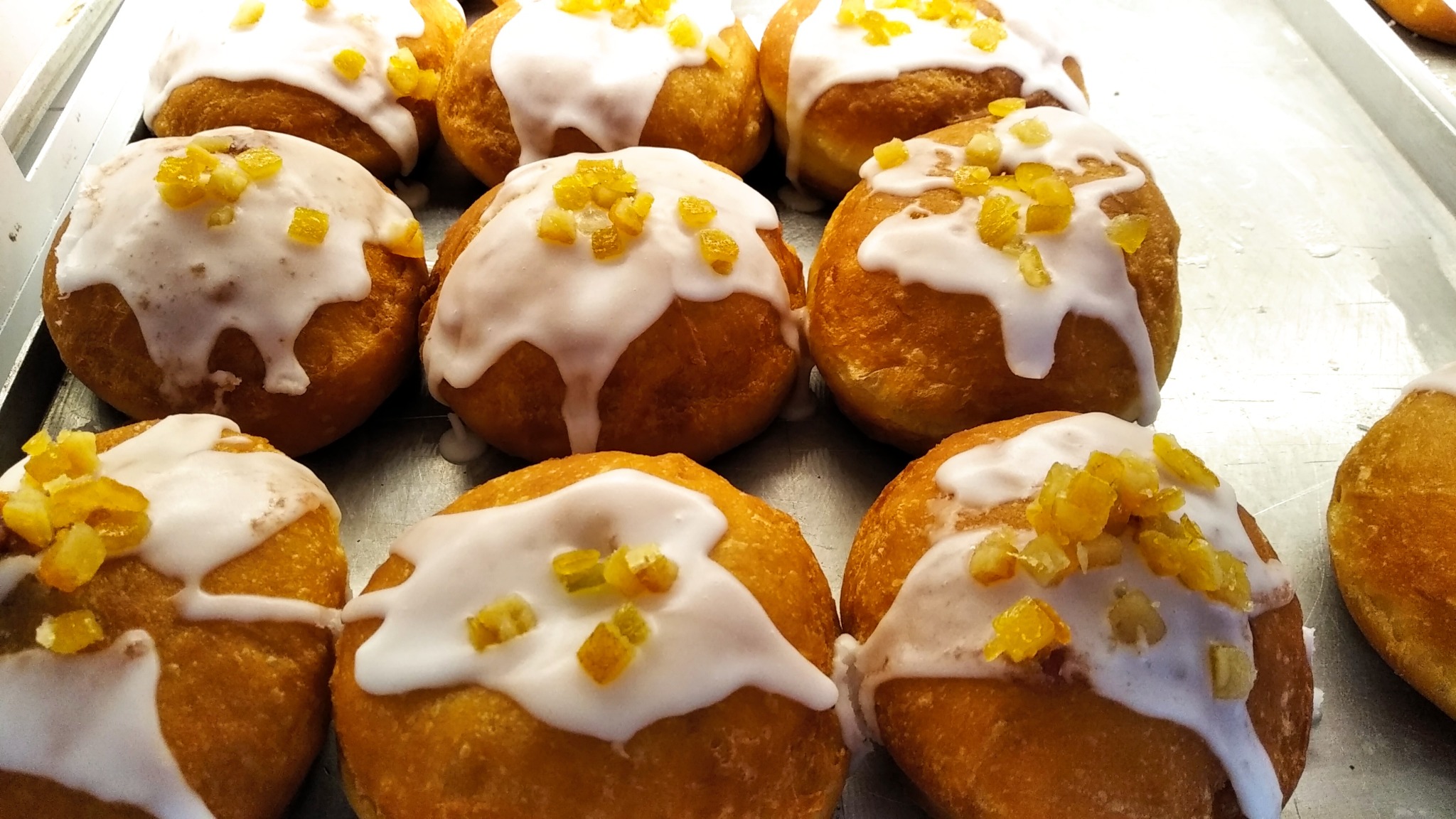 Pączki z białym lukrem i kandyzowaną skórką pomarańczową na metalowej tacy.