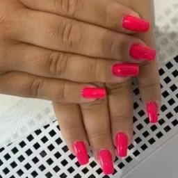 Dłonie z pomalowanymi na jaskrawy róż paznokciami o kwadratowym kształcie, ułożone na tle w czarno-białą kratkę.