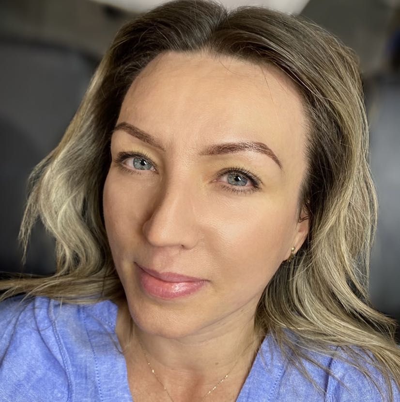 Portret kobiety z delikatnym makijażem, podkreślone brwi, subtelny błyszczyk na ustach, jasne oczy i blond włosy z odrostami.