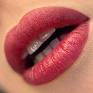 Zbliżenie na usta z trwałym makijażem. Widoczny efekt ombre, od ciemniejszego odcienia na konturze do jaśniejszego wewnątrz. Zauważalne delikatne zmarszczki na powierzchni ust.