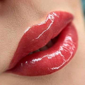 Zbliżenie na usta z błyszczącym, czerwonym makijażem, widoczne drobne zmarszczki wokół ust.