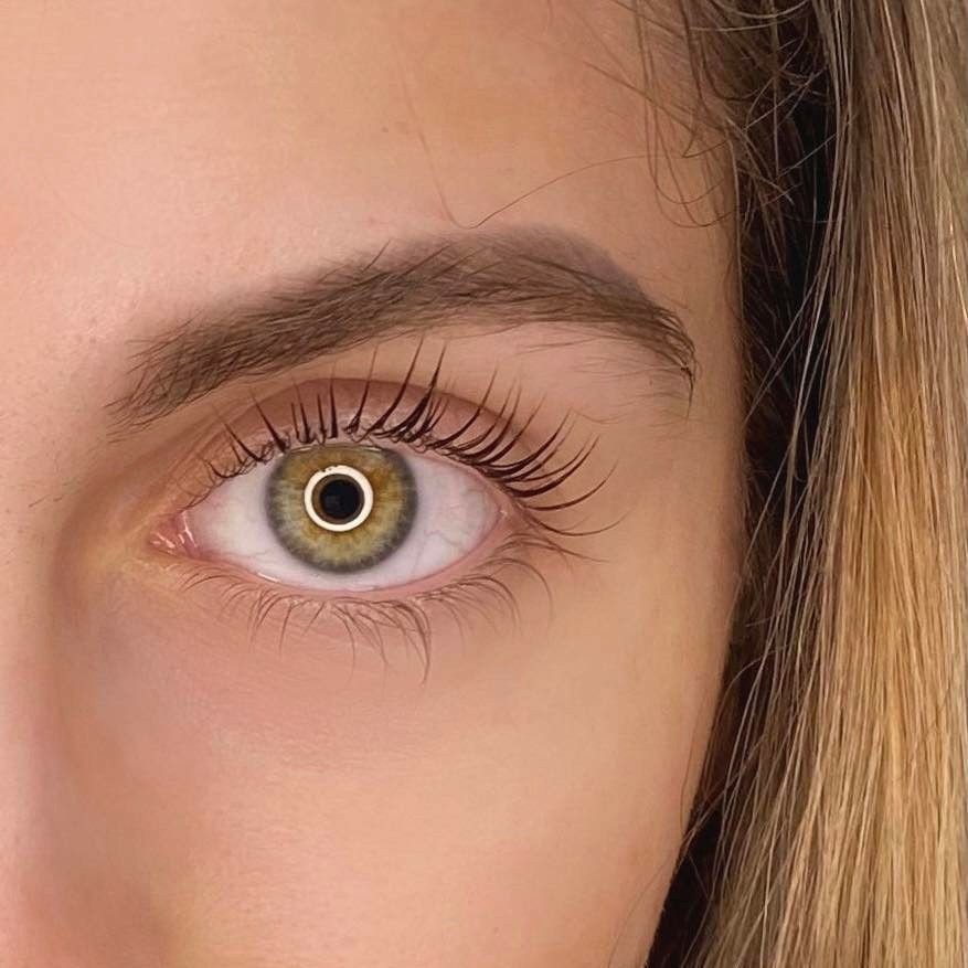 Zbliżenie na oko z widocznymi, wydłużonymi i podkręconymi rzęsami, jasna karnacja, widoczne pojedyncze włoski brwi, zielono-szare tęczówka oka.