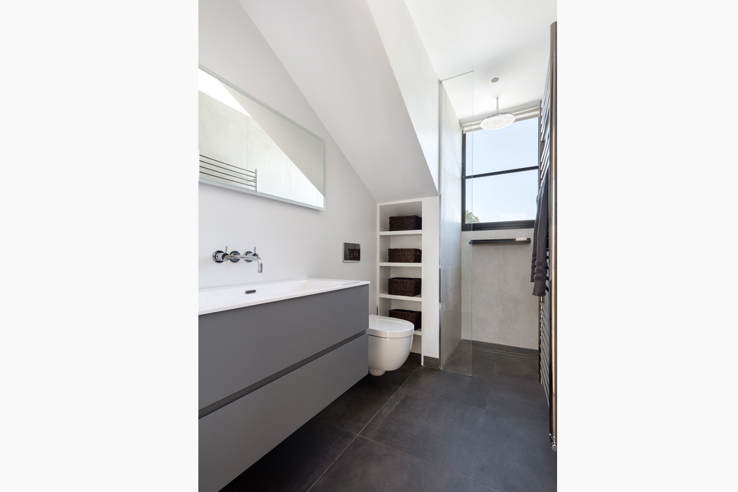 Nowoczesna łazienka na poddaszu z szarą szafką pod umywalką, toaletą w zabudowie, kabiną prysznicową z deszczownicą i oknem dachowym.