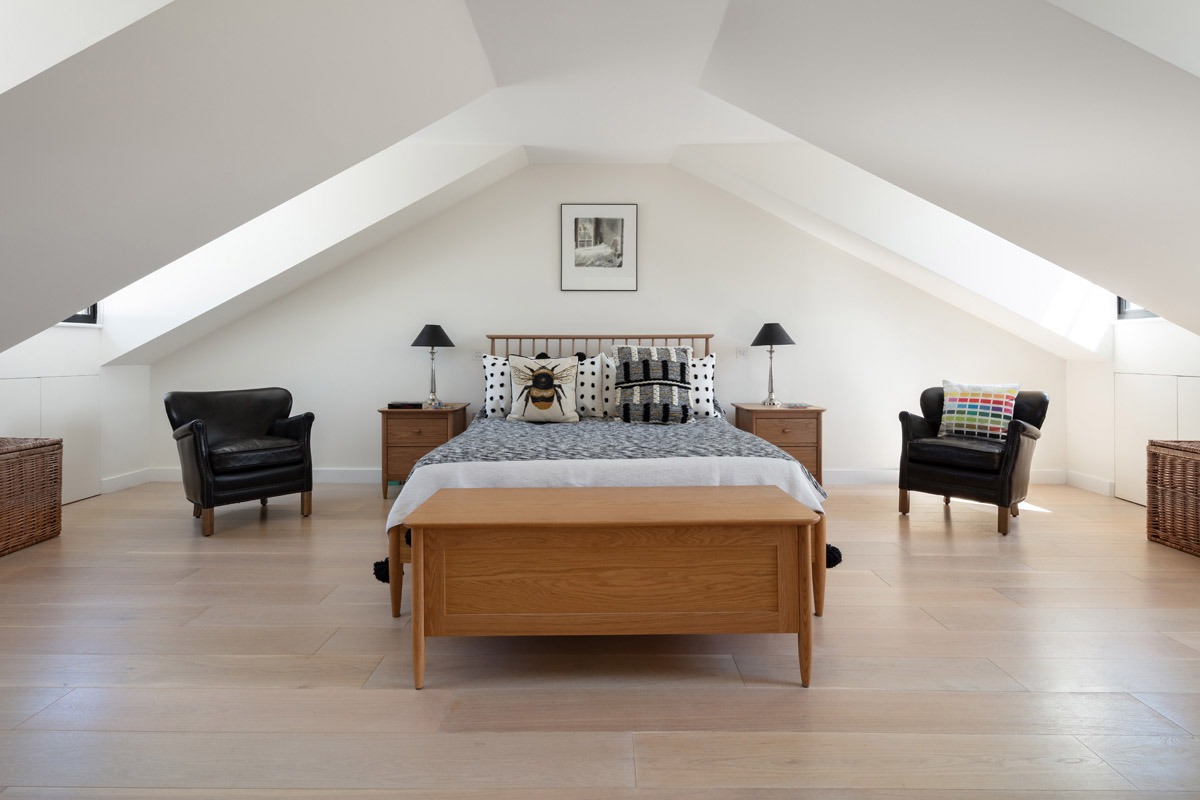 Jasna sypialnia na poddaszu w Pobierowie z łóżkiem, drewnianą komodą, dwiema skórzanymi fotelami i oknami dachowymi.